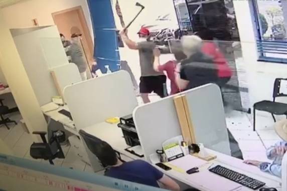 Conforme as imagens de monitoramento, o homem chegou ao local, golpeou a porta de vidro do estabelecimento, que se estilhaçou e atingiu uma mulher.