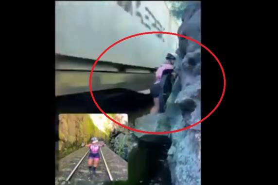 As imagens mostram a ciclista em um pequeno espaço entre o trem e as pedras, para não ser atropelada