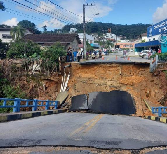Mulher de 60 anos estava a caminho de escola para buscar a neta quando ponte caiu em Brusque após chuva. Ele se segurou para não cair no buraco e não teve ferimentos graves.
