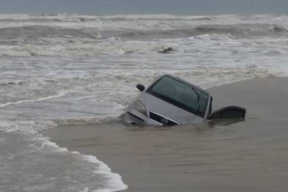 De propriedade de casal de idosos vítima de golpe, carro foi abandonado à beira-mar e, com a maré alta, está sendo engolido pela areia e pela água do mar