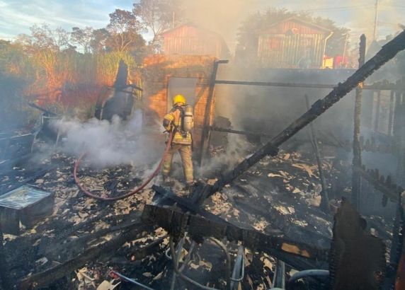 Casa de madeira foi completamente consumida pelas chamas; suspeita inicial aponta para curto-circuito em tomada da cozinha